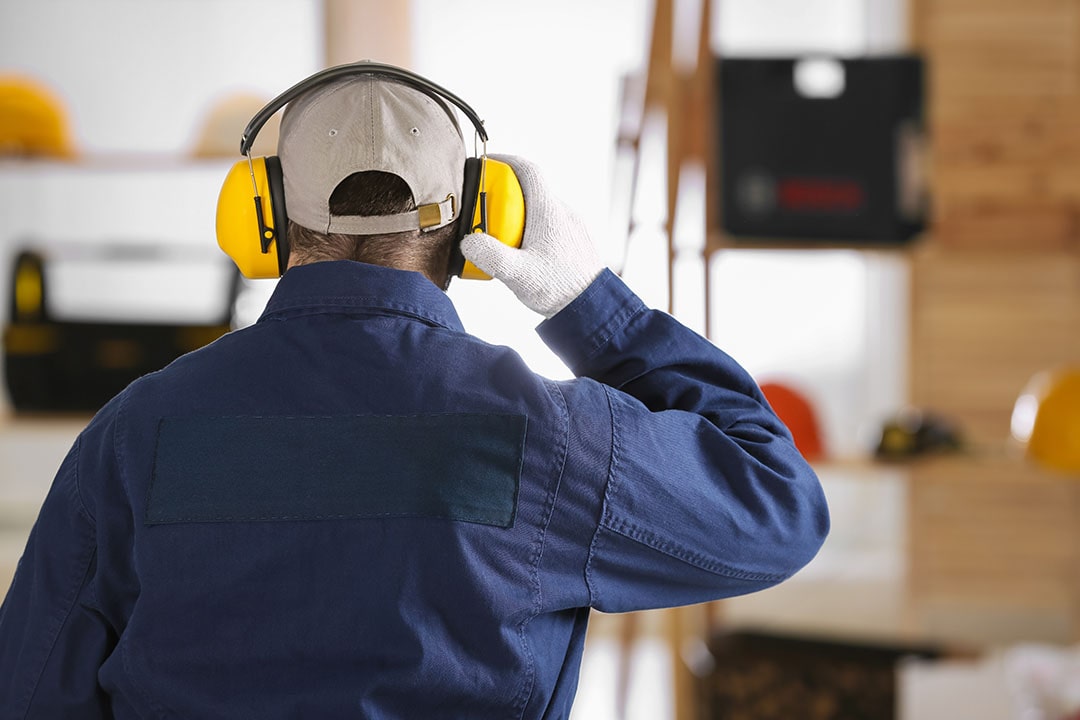Worker wearing safety headphones for hearing protection indoors as industrial hygiene protocol, back view.