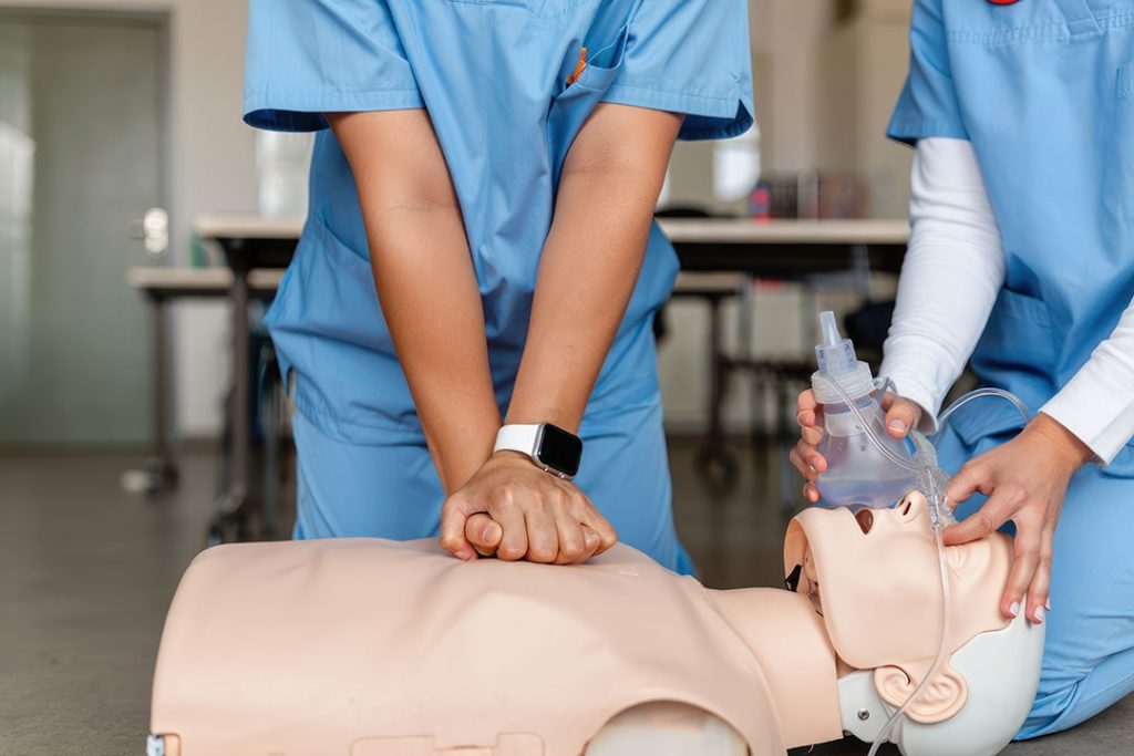 Two healthcare professionals practicing CPR and ventilation on a resuscitation mannequin in a clinical training room